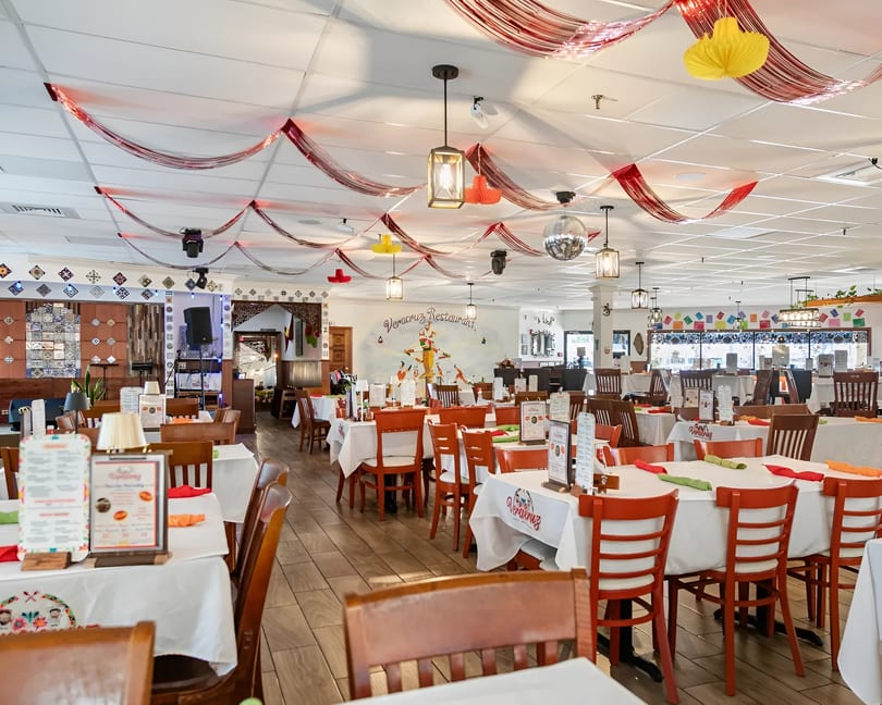 Spacious Veracruz Restaurant dining room with white tablecloths, orange chairs, and festive ceiling decorations.