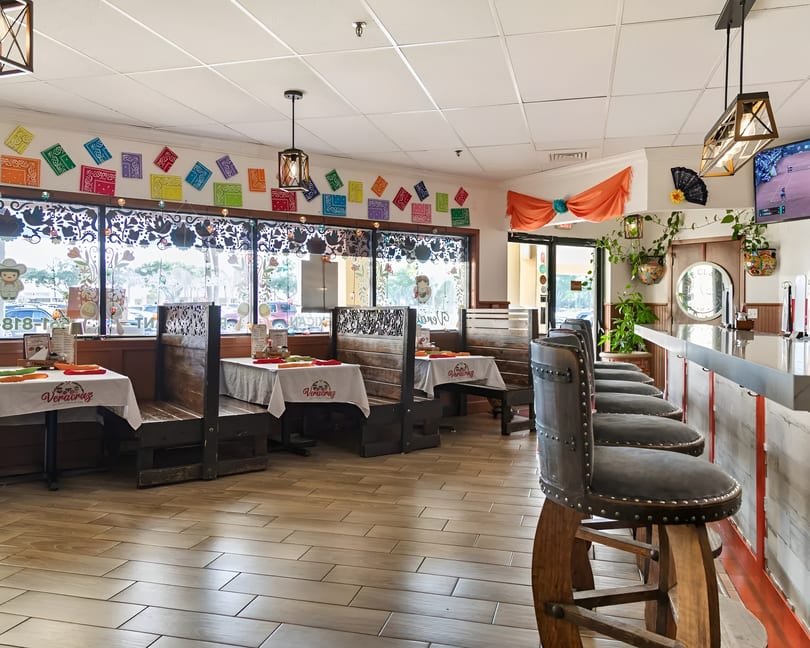 Interior of a vibrant Mexican restaurant with colorful decor, wooden booths, and a bar with studded stools.