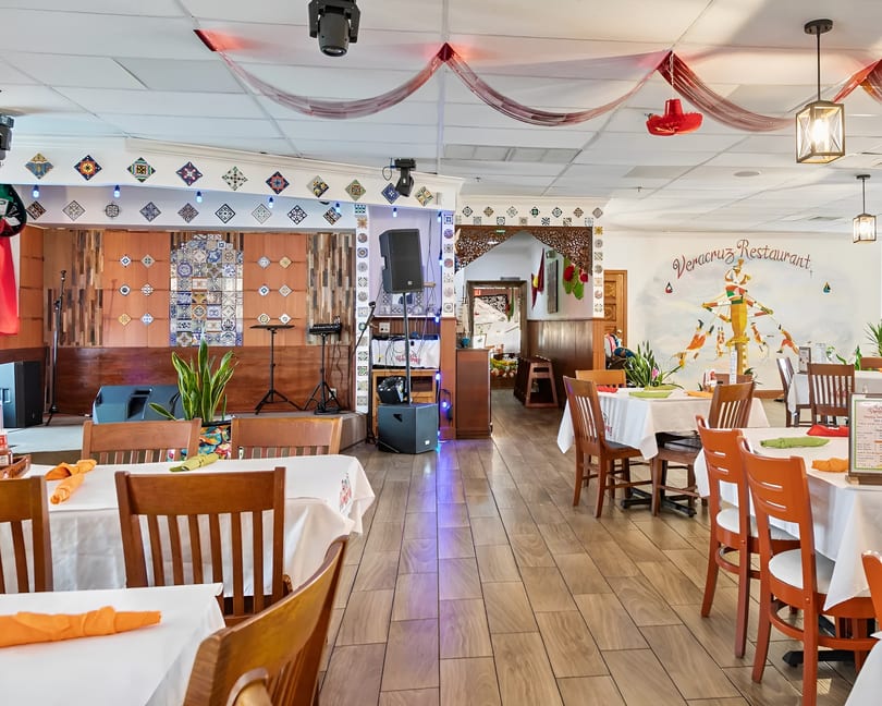 Interior of Veracruz Restaurant with dining tables, a stage, and a colorful mural on the wall.